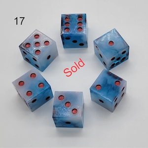May include: Six translucent dice with a swirling blue and white marbled pattern and recessed red pips. The number 17 is printed in black in the upper left corner, and the word Sold is printed in red in the center of the arrangement.