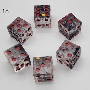 May include: A set of five six-sided dice arranged in a circle, labeled with the number 18. Each die is made of a translucent material with a mottled black and grey pattern, featuring recessed circular pips filled with a bright red color.