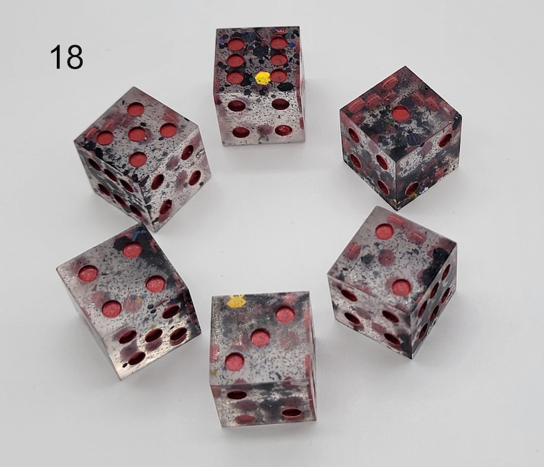 May include: A set of five six-sided dice arranged in a circle, labeled with the number 18. Each die is made of a translucent material with a mottled black and grey pattern, featuring recessed circular pips filled with a bright red color.