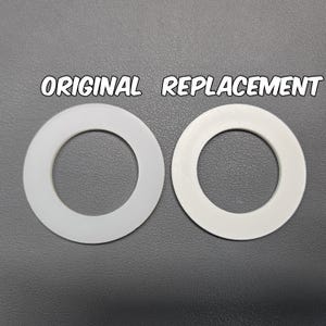 May include: Two white circular washers are displayed side by side. The left washer is labeled ORIGINAL and the right washer is labeled REPLACEMENT. Both items are flat, ring-shaped components with a smooth surface and a central circular opening.