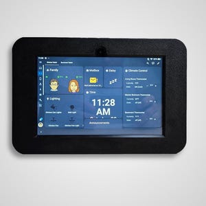 May include: A black framed tablet displaying a smart home control interface. The screen shows various icons for family, lighting, and climate control, with the time displayed as 11:28 AM. The tablet is mounted on a white wall.
