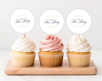 May include: Three cupcakes with white and pink frosting, each topped with a circular sign that reads "Tea Party." The cupcakes sit on a wooden board. The cupcakes have a yellow cake base and are in paper liners.