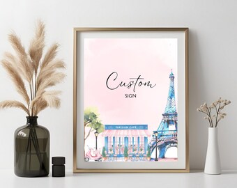 Könnte beinhalten: Ein gerahmter Aquarelldruck mit einem Pariser Café, dem Eiffelturm und einem rosa Roller. Die Worte "Custom Sign" sind in eleganter Schrift geschrieben. Das Kunstwerk ist vor einem zartrosa Hintergrund in Gold gerahmt.