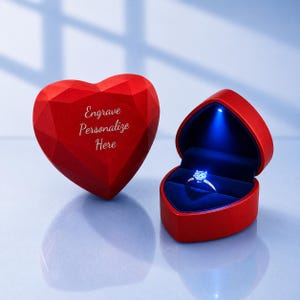 May include: A red heart-shaped ring box with a faceted exterior and the text Engrave Personalize Here, paired with an open matching box containing a silver ring illuminated by a small blue LED light inside the dark blue velvet interior lining.