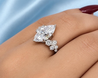 May include: A silver-toned ring featuring a large marquise-cut center stone and a cluster of five smaller round-cut stones arranged along one side of the band. The metal setting is polished and reflective, showcasing clear, faceted gemstones.