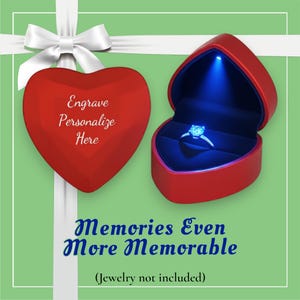 May include: A red heart-shaped jewelry box with a ring inside, illuminated by a blue light. The box is open, revealing the ring. The text "Engrave Personalize Here" is on a closed heart-shaped box. The text "Memories Even More Memorable" is also present.