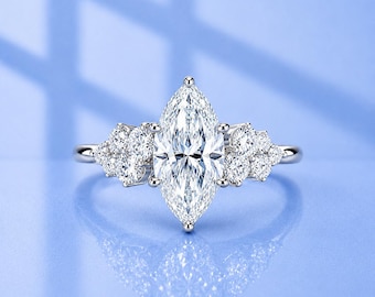 Peut inclure: Une bague argentée ornée d'une grande pierre centrale transparente taille marquise, entourée d'un groupe de trois petites pierres rondes transparentes de chaque côté, montée sur un anneau en métal poli reflétant la lumière.