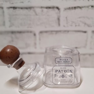 May include: A clear glass bottle with a wooden stopper and a label that reads "Tequila 100% Agave Silver Patron".