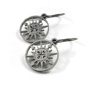 May include: A pair of silver compass earrings with a circular design featuring a compass rose with the directions N, S, E, and W. The earrings have a hoop design.