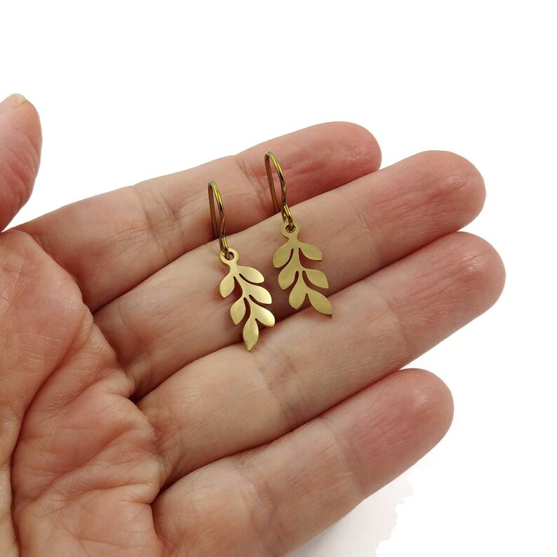 May include: A pair of gold leaf earrings with a delicate, branch-like design. The earrings are made of metal and have a simple, elegant style.