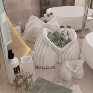 May include: White ceramic bathroom organiser with a wavy design, holding rolled towels and small bottles. The organiser is on a white countertop next to a white sink.