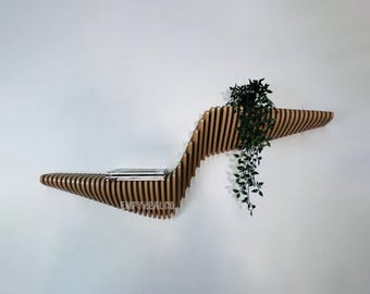 Può includere: Un ripiano a muro in legno con un design ondulato. Il ripiano ha una piccola pianta in un vaso sulla parte superiore e una pila di libri sul ripiano inferiore. Il ripiano è realizzato in legno marrone chiaro e ha una finitura naturale.