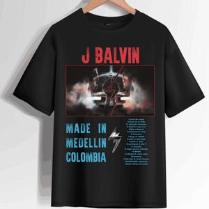 Pode incluir: Camiseta preta com um gr&aacute;fico branco de J Balvin em um carro com o texto "Made in Medellin Colombia" e uma lista de t&iacute;tulos de m&uacute;sicas do &aacute;lbum.