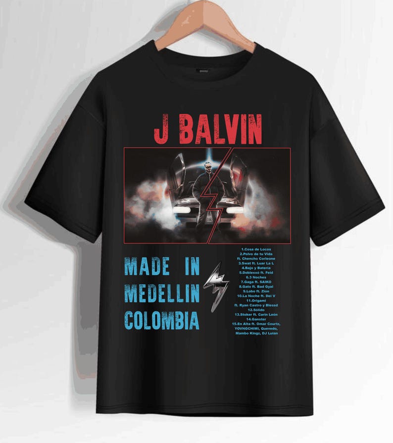 Pode incluir: Camiseta preta com um gr&aacute;fico branco de J Balvin em um carro com o texto "Made in Medellin Colombia" e uma lista de t&iacute;tulos de m&uacute;sicas do &aacute;lbum.