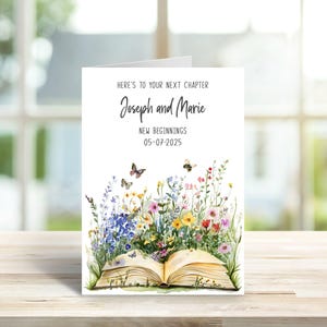 Könnte beinhalten: Eine Grußkarte mit dem Text "Here's to your next chapter" und den Namen "Joseph and Marie". Die Karte zeigt ein offenes Buch mit einer Aquarellillustration von bunten Wildblumen, Schmetterlingen und Bienen. Das Datum "05-07-2025" ist ebenfalls enthalten.