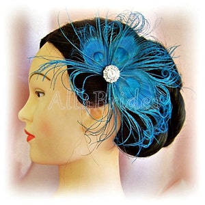 Op de afbeelding: Een haar kam met teal blauwe pauwenveren met een strass accent. De kam wordt gedragen in het haar van een vrouw.