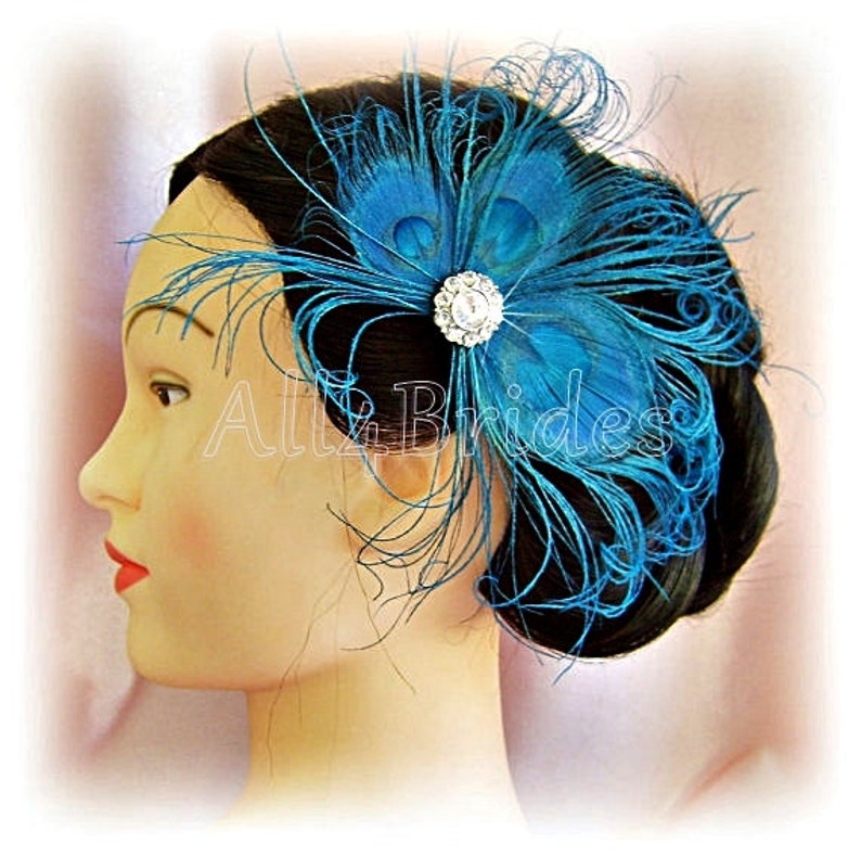 Op de afbeelding: Een haar kam met teal blauwe pauwenveren met een strass accent. De kam wordt gedragen in het haar van een vrouw.