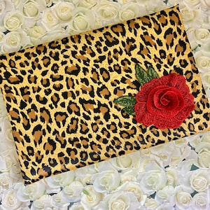 May include: A leopard print clutch purse with a red fabric rose appliqué.