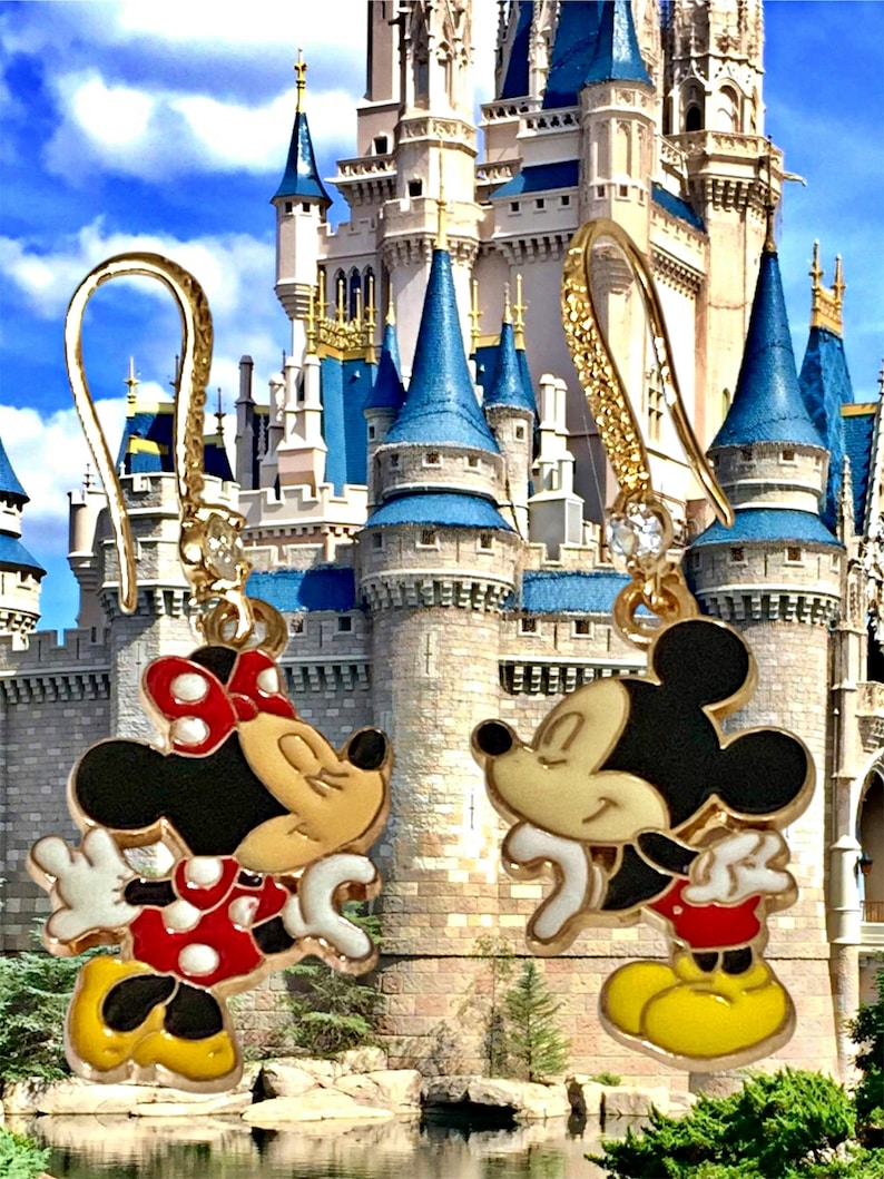 K&ouml;nnte beinhalten: Goldfarbene Mickey Mouse und Minnie Mouse Ohrh&auml;nger. Minnie tr&auml;gt ein rot-wei&szlig; gepunktetes Kleid und eine Schleife. Mickey tr&auml;gt rote Shorts und gelbe Schuhe. Im Hintergrund ist ein Schloss zu sehen.