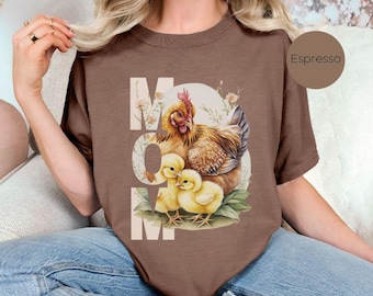 May include: A brown t-shirt with a graphic of a hen and chicks. The graphic is surrounded by flowers and the word "MOM" is printed in white on the shirt.