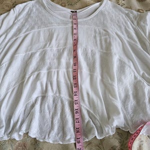 以下が含まれることがあります： 白いフローイングトップ、花の刺繍とラウンドネックが特徴です。 ピンクのメジャーで測定すると、長さは約48cmです。 生地は柔らかく、軽量に見えます。