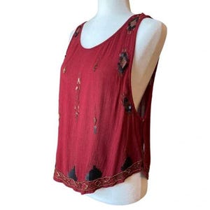 May include: A red sleeveless top with black and gold embellishments. The top has a scoop neck and is made from a lightweight fabric. It is decorated with sequins and small gold beads. The garment is designed to be worn as a tank top.