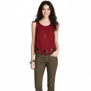 May include: A sleeveless burgundy top with decorative beading and embellishments. The top is paired with olive green trousers. The model is wearing a gold bracelet.