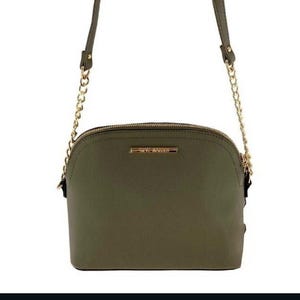 May include: Olive green crossbody bag with a gold chain strap. The bag has a rounded shape with a gold zipper and a small gold rectangular logo that reads "STEVE MADDEN". The bag is made of a smooth material.