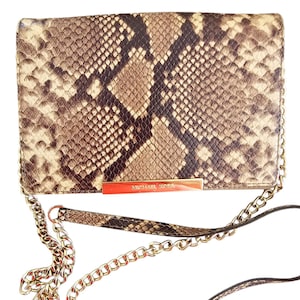 May include: A rectangular clutch with a snakeskin pattern in shades of brown, tan, and black. The clutch features a gold-tone chain strap and a gold bar with the "MICHAEL KORS" logo.
