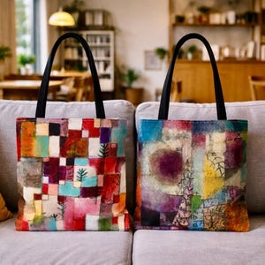 Pode incluir: Duas sacolas com alças pretas e designs de arte abstrata coloridos. Uma sacola apresenta um patchwork de quadrados vermelhos, laranja e azul com formas de árvores verdes. A outra sacola tem um design azul, roxo e amarelo.