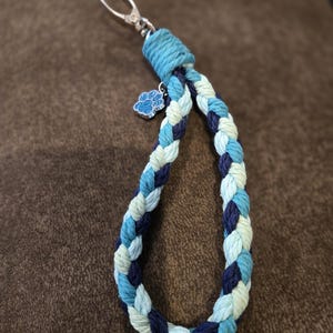 May include: A braided key chain with a silver paw print charm. The keychain is made of blue, white, and navy blue rope.
