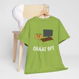May include: A green t-shirt featuring a cartoon illustration of a smiling orange food item seated at a desk with a computer and mouse. The text "CHAAT GPT" is printed in white below the image.