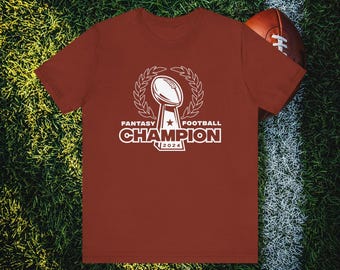 Op de afbeelding: Een maroon t-shirt met een witte afbeelding van een voetbaltrofee en de tekst "Fantasy Football Champion 2024".