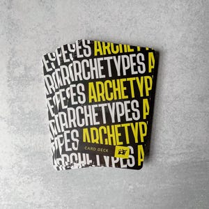 May include: A stack of black and yellow card decks with the text "Archetypes" repeated on each card. The text "Card Deck" is also visible on the top card.