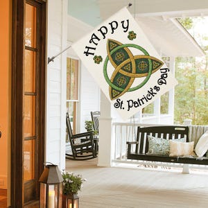 Könnte beinhalten: Eine rechteckige St. Patrick's Day-Flagge mit den Worten "Happy St. Patrick's Day" in schwarzer Schrift. Die Flagge zeigt ein grünes und goldenes keltisches Knotendesign. Die Flagge hängt an einer Veranda.
