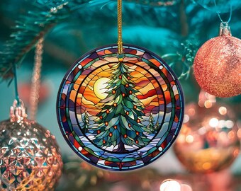 Puede incluir: Adorno navideño redondo con diseño de vidriera. El adorno presenta una imagen central de un árbol de Navidad, un sol poniente y un paisaje nevado. El borde es una mezcla de rojo, azul y verde. Cuelga de un hilo dorado.