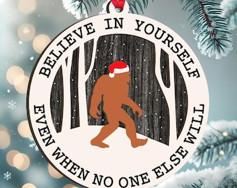 May include: A round wooden Christmas ornament with the text "BELIEVE IN YOURSELF EVEN WHEN NO ONE ELSE WILL". The ornament features a brown Bigfoot wearing a Santa hat walking through a snowy forest scene.