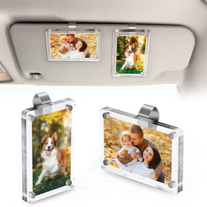 Könnte beinhalten: Transparente Acryl-Fotorahmen mit silbernen Clips, die Familienfotos und einen Hund zeigen. Die Rahmen sind zur Befestigung an einer Sonnenblende im Auto konzipiert. Die Fotos zeigen eine Familie und einen Hund in der Natur.