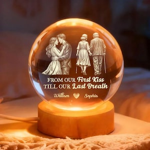 Puede incluir: Una bola de cristal brillante con una escena romántica grabada de una pareja y una pareja de ancianos tomados de la mano. El texto dice "FROM OUR First Kiss TILL OUR Last Breath" con los nombres "William" y "Sophia". La bola está sobre una base de madera.