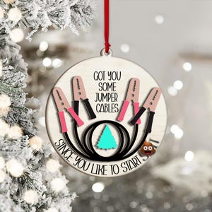 May include: A round Christmas ornament with a red ribbon. The ornament features a design of jumper cables with the text "GOT YOU SOME JUMPER CABLES SINCE YOU LIKE TO START". A turquoise tree and a poop emoji are also included.