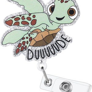 May include: A light green turtle-shaped badge reel with a smiling face and the word "DUUUUDE" in black. The turtle has brown spots and a glittery silver border. The reel has a clear plastic clip and a metal retractable cord.