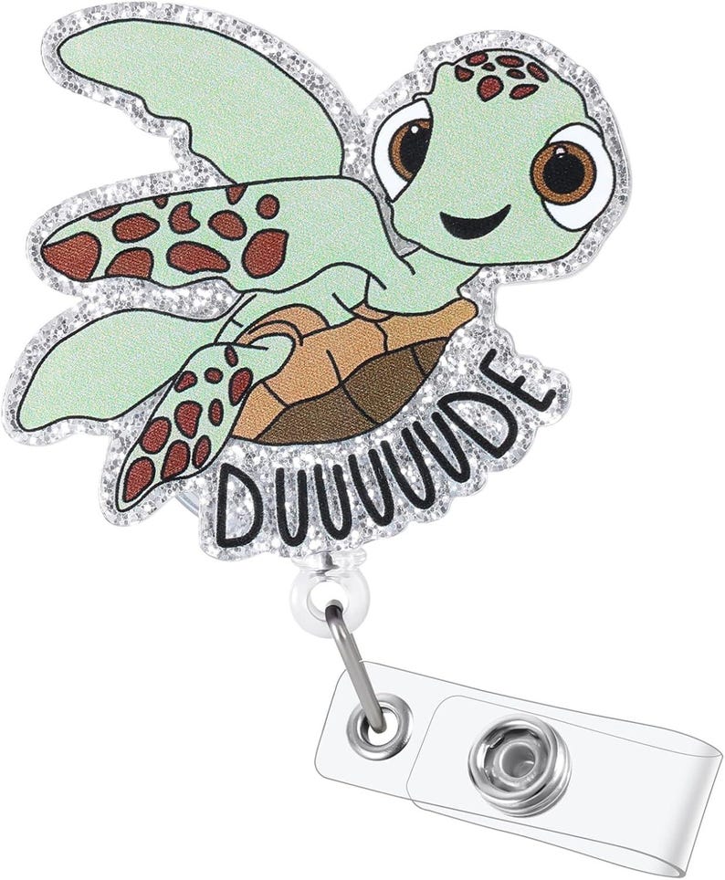 May include: A light green turtle-shaped badge reel with a smiling face and the word "DUUUUDE" in black. The turtle has brown spots and a glittery silver border. The reel has a clear plastic clip and a metal retractable cord.
