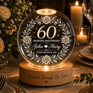 以下が含まれることがあります： 60 DIAMOND ANNIVERSARY、JohnとMary、TOGETHER SINCE 1966の文字と花のリースが刻印された球状のガラス製ライト。土台は明るい木製の円柱で、Cherished Through The Yearsという文字とハートのマークが刻印されています。