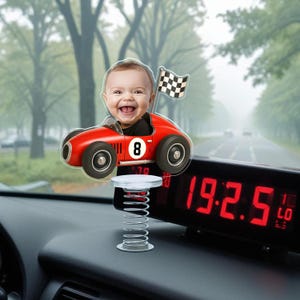 May include: A smiling baby in a red race car with the number 8 and a checkered flag. The car is mounted on a spring. A digital clock with red numbers displays 19:25.