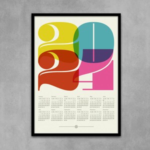 May include: A colorful calendar for the year 2021 with a graphic design of the numbers 2021 in overlapping circles of yellow, red, teal, purple, and pink. The calendar includes all 12 months of the year.