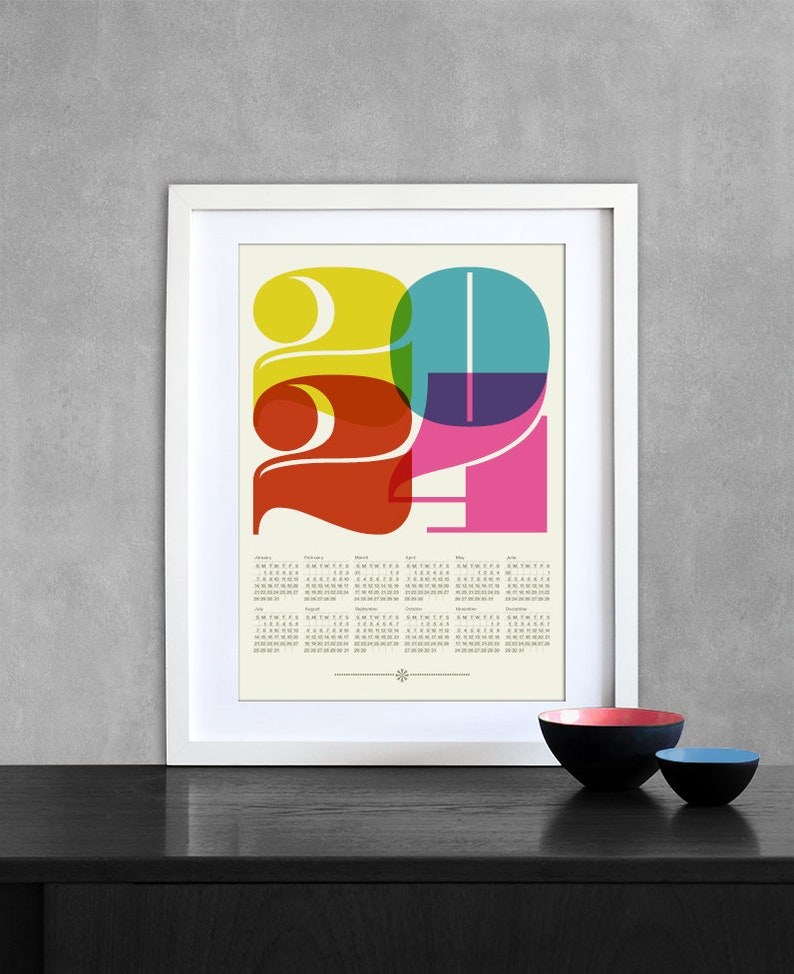 May include: A white framed print of a 2021 calendar with a colorful graphic design of the year 2021. The numbers are layered in overlapping circles of yellow, orange, red, purple, and blue.