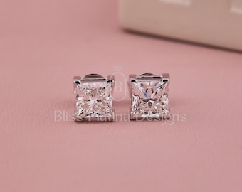 Può includere: Un paio di orecchini a lobo color argento con pietre trasparenti a taglio quadrato e superficie sfaccettata. Gli orecchini sono posizionati fianco a fianco e il testo Bliss Platinum Designs è visibile al centro tra i due gioielli.