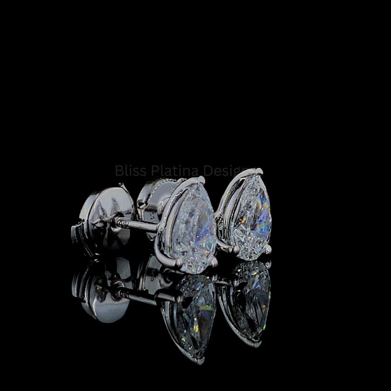 Pu&ograve; includere: Un paio di orecchini a lobo color argento con pietre trasparenti sfaccettate a forma di pera incastonate nel metallo. Il testo Bliss Platina Design &egrave; visibile al centro su sfondo nero. Il design include chiusure a perno sul retro.