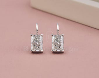 Può includere: Un paio di orecchini pendenti color argento con pietre rettangolari trasparenti sfaccettate montate su griffe in metallo. Ogni orecchino presenta un sottile perno metallico verticale che si estende dalla parte superiore. Testo Bliss Platinum Designs.