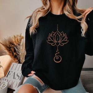 May include: Black sweatshirt with a brown lotus flower design. The lotus flower is stylized and has a stem with a swirl at the bottom.